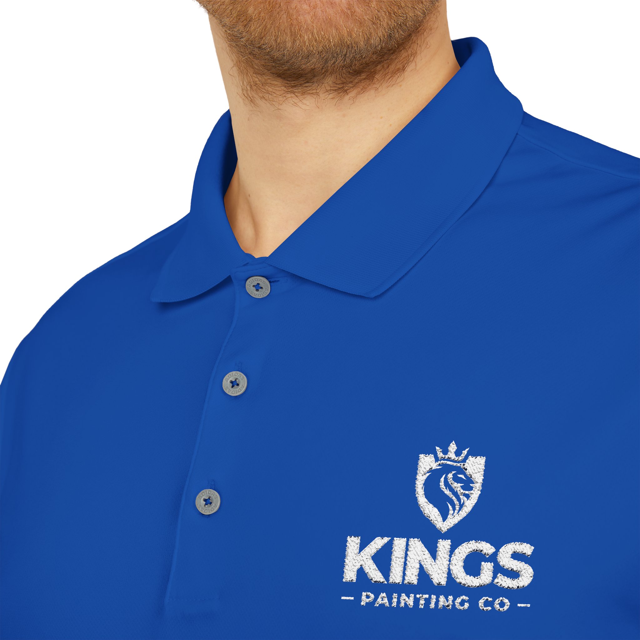 A person wearing a royal blue Kings Painting Co. Performance Polo by Under Armour®, featuring a white KINGS PAINTING CO logo and a crowned lion emblem on the left chest.