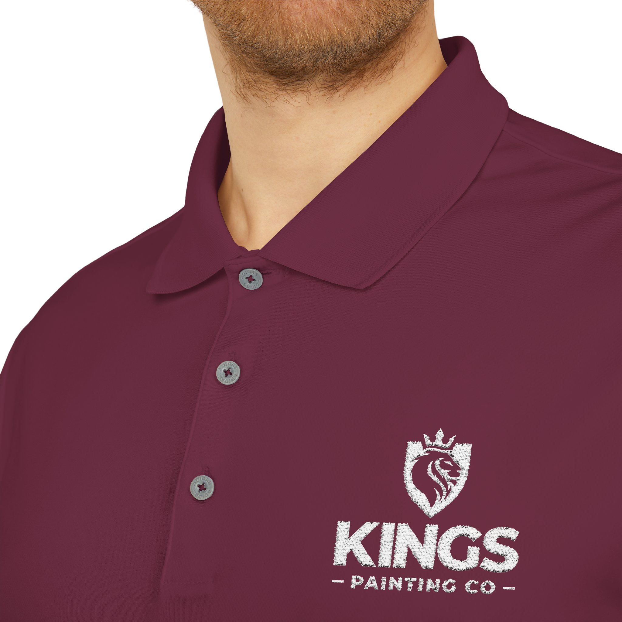A person wearing the Kings Painting Co. Performance Polo by Under Armour®, featuring gray buttons and a white lion logo with a crown above the "KINGS PAINTING CO" text on the left chest area.