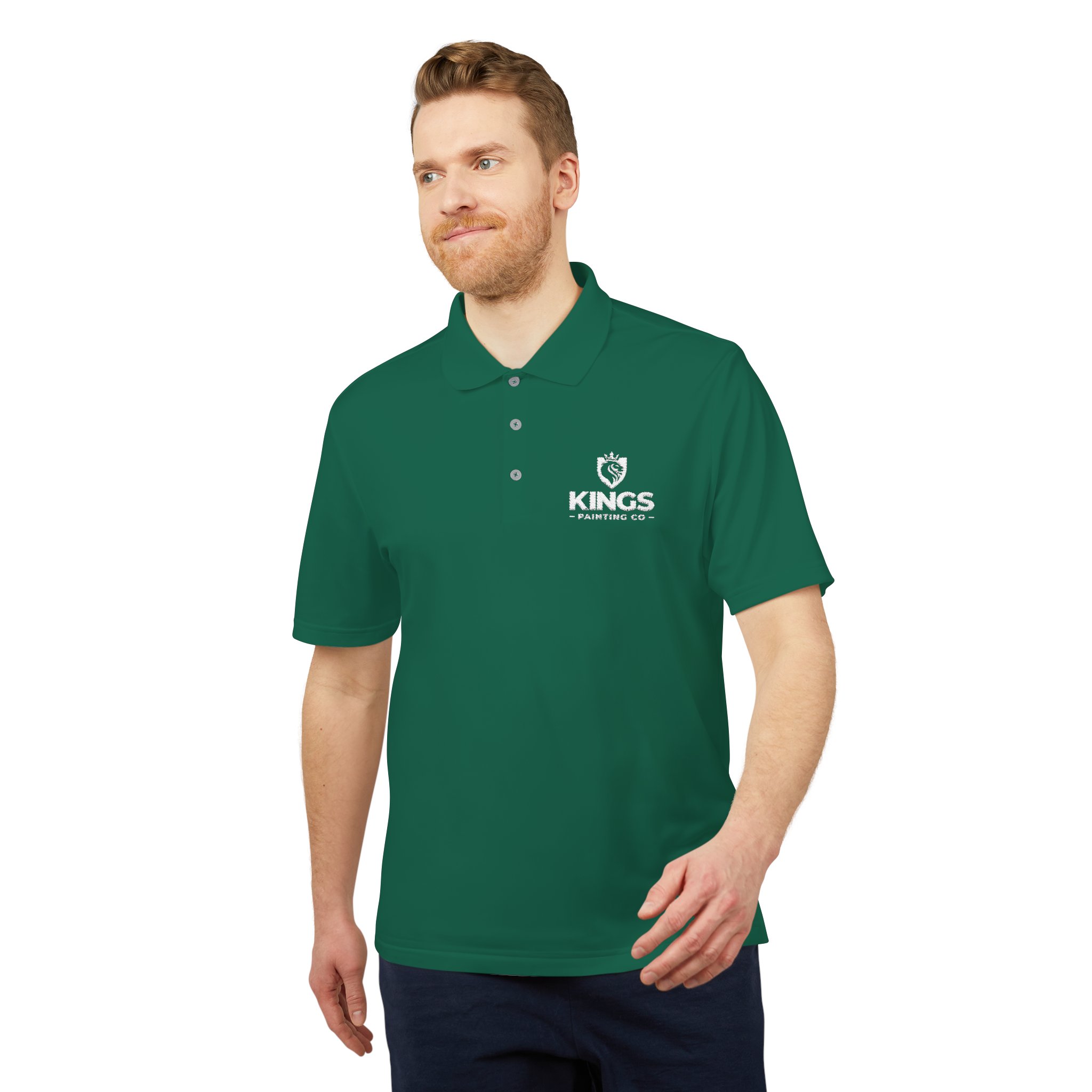 A light-skinned, bearded man is wearing a green Kings Painting Co. Performance Polo by Under Armour® with a white logo on the left chest. He appears to be walking and is smiling slightly.