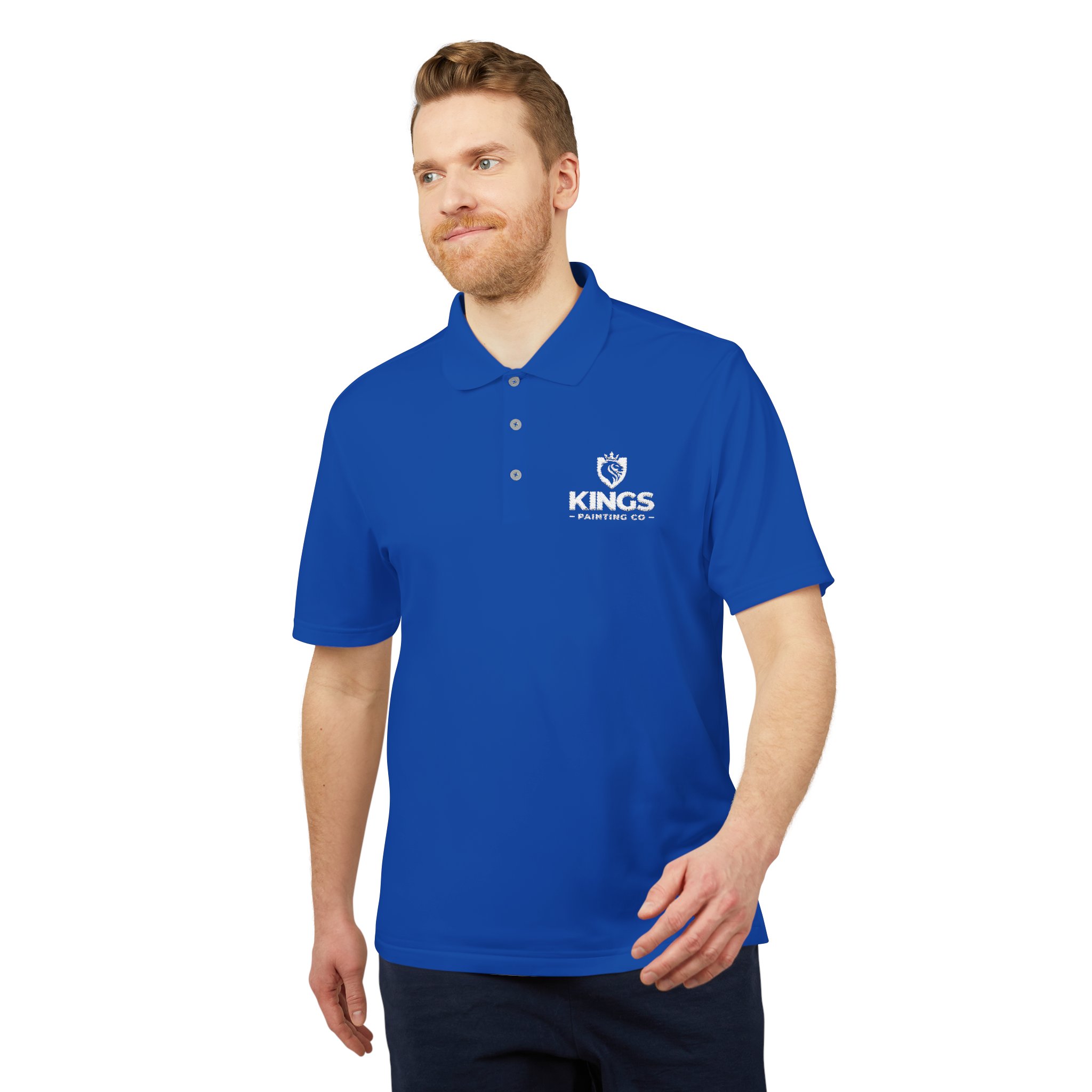 A man wearing a royal blue Kings Painting Co. Performance Polo by Under Armour®, featuring a white logo, stands against a white background, smiling with one arm slightly extended.